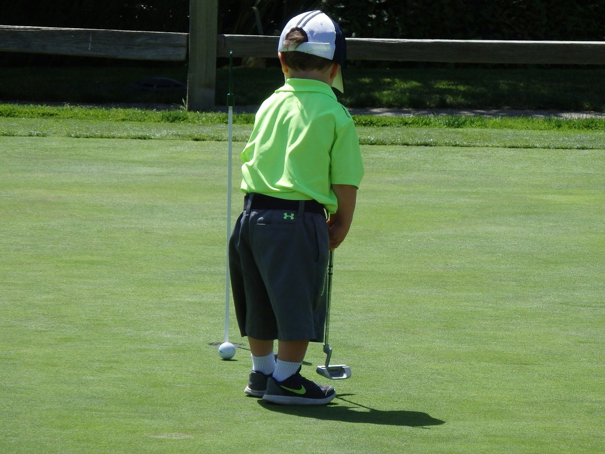 Jeune garçon vu de dos sur un green, putter en main